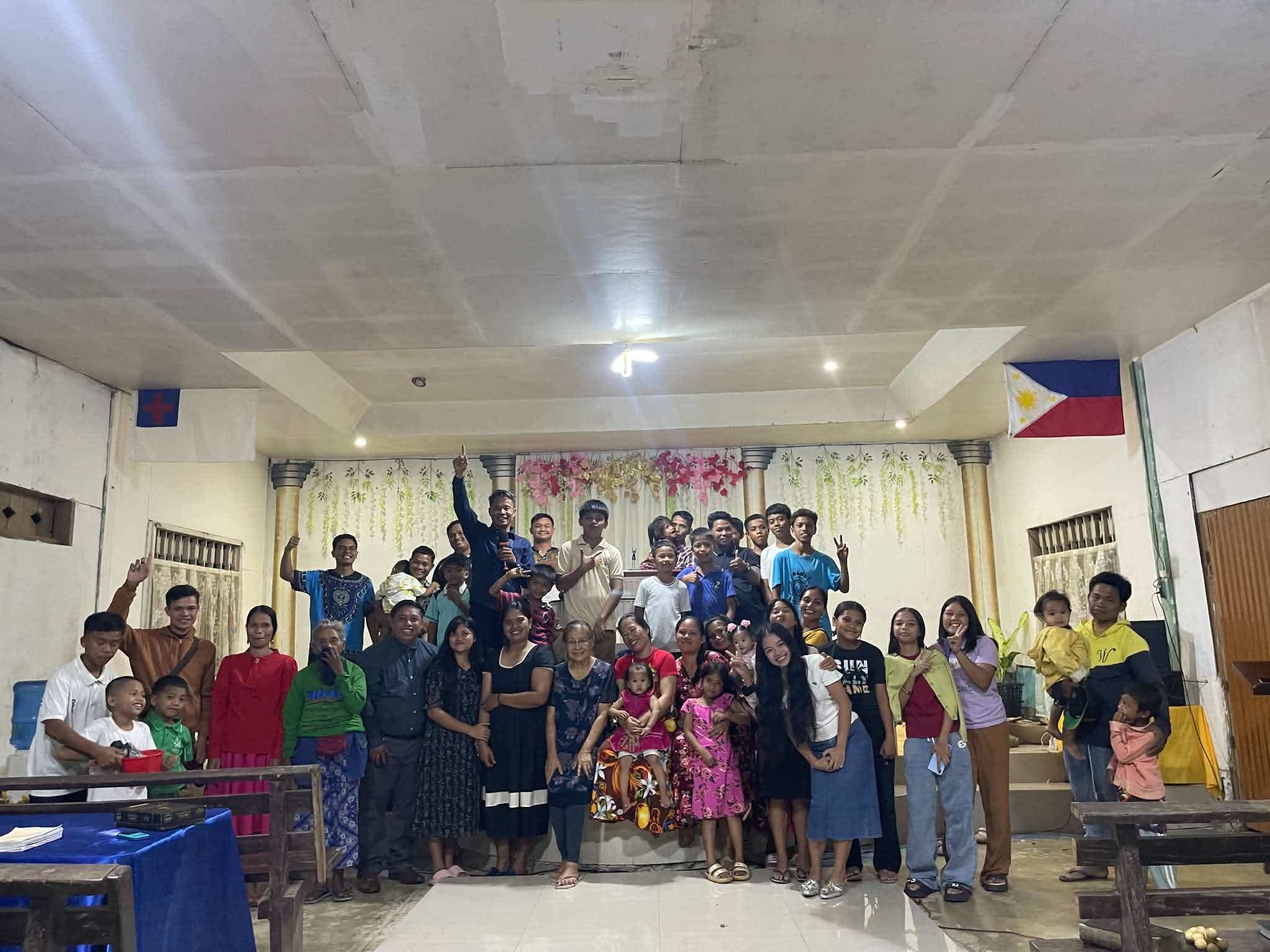 Adults and children gathered for a group photo inside a church hall