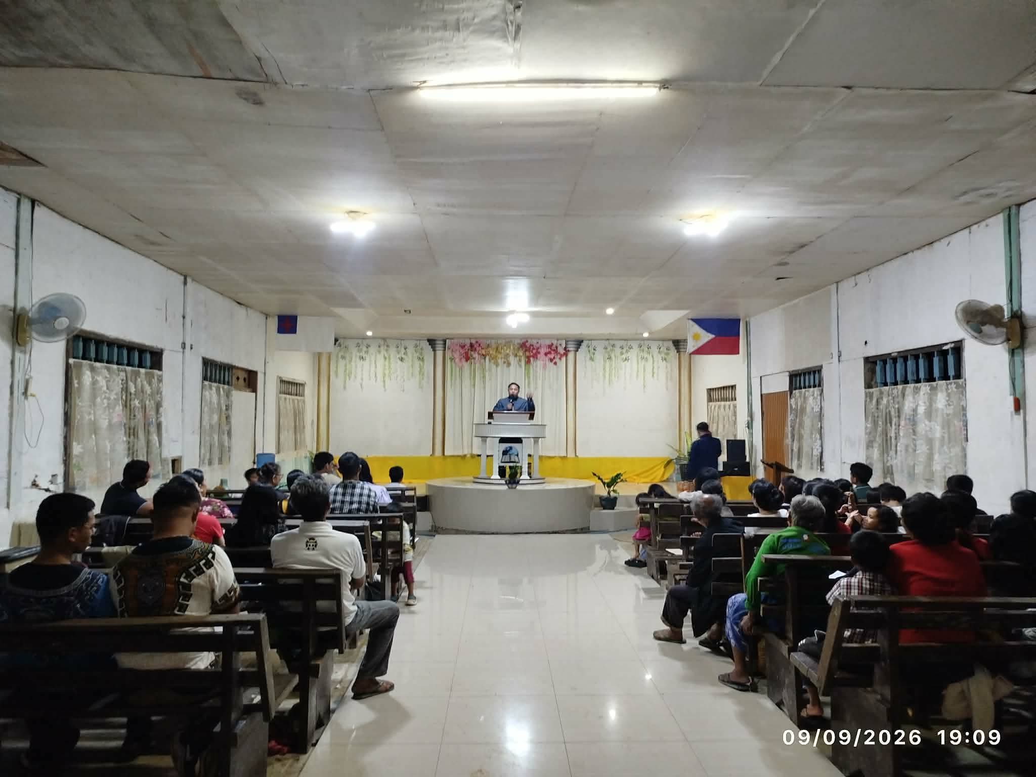 Congregation seated in a church hall while a speaker stands at the front