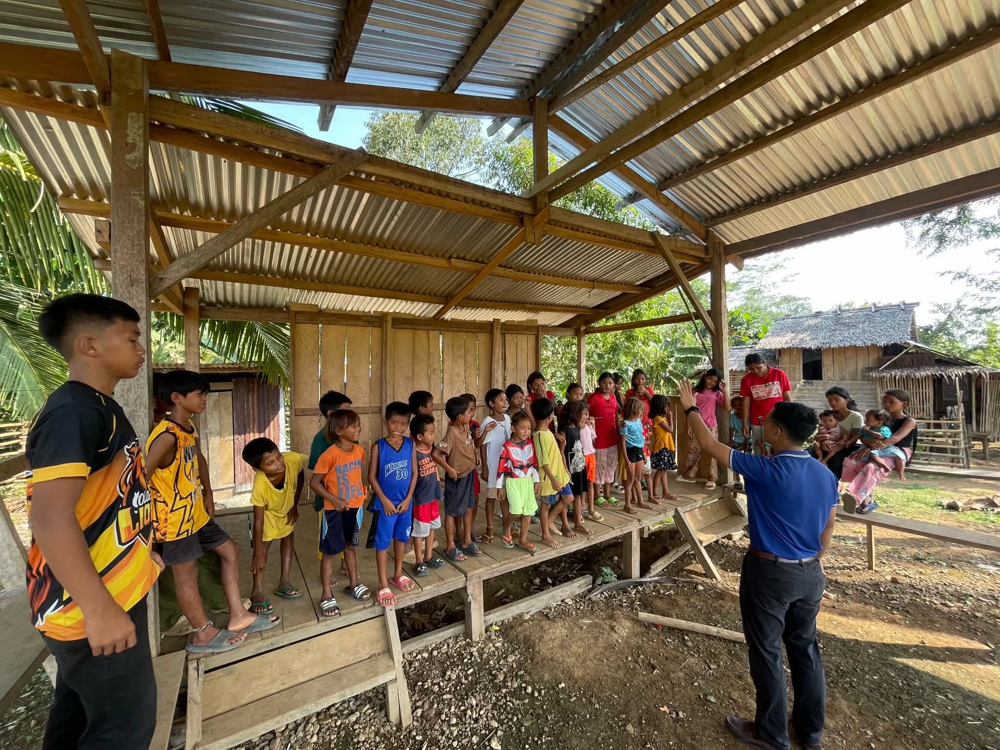 An adult leading children in a group activity in an open-sided shelter