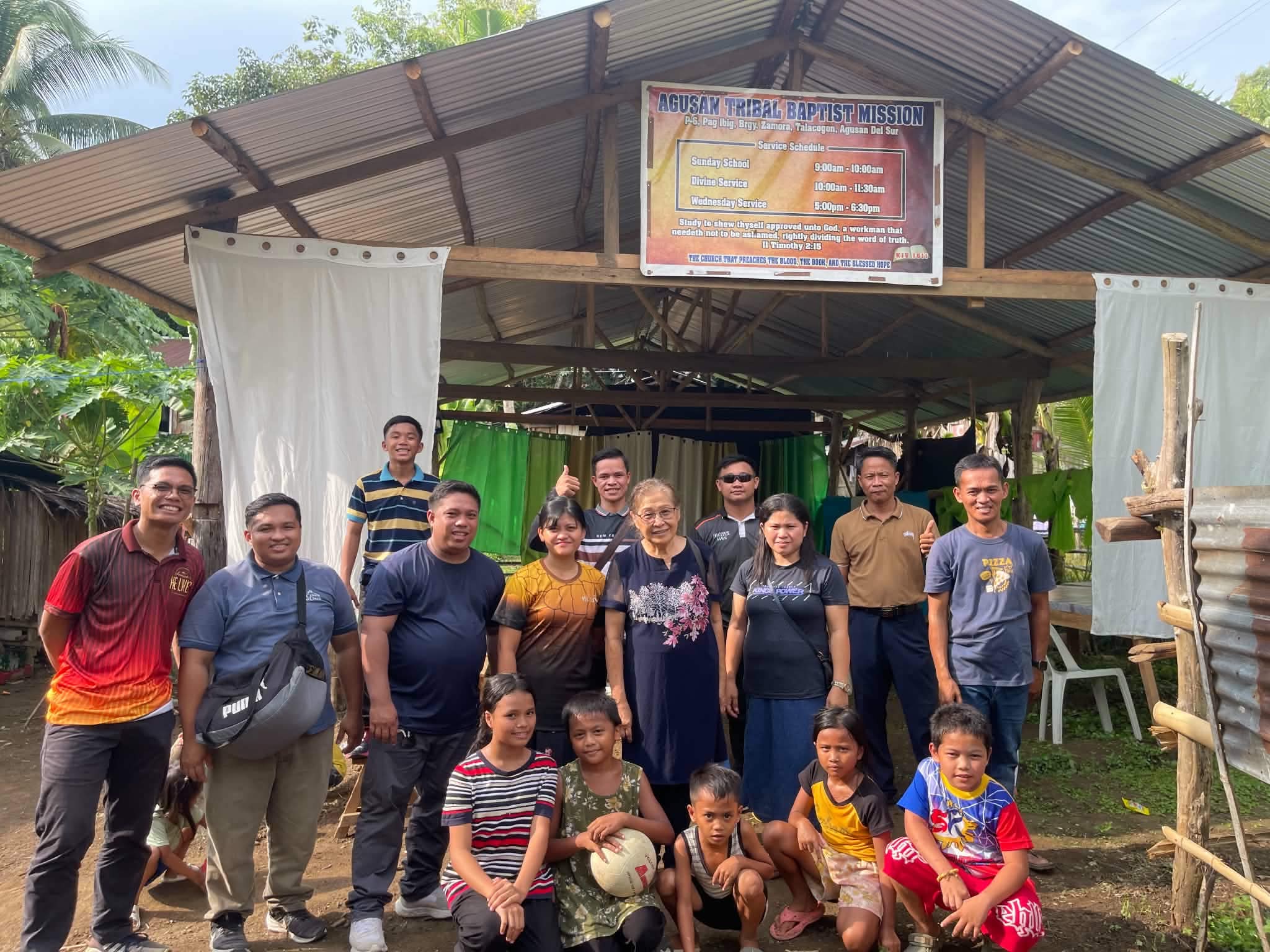 Visitors and community members posing outside a small church building
