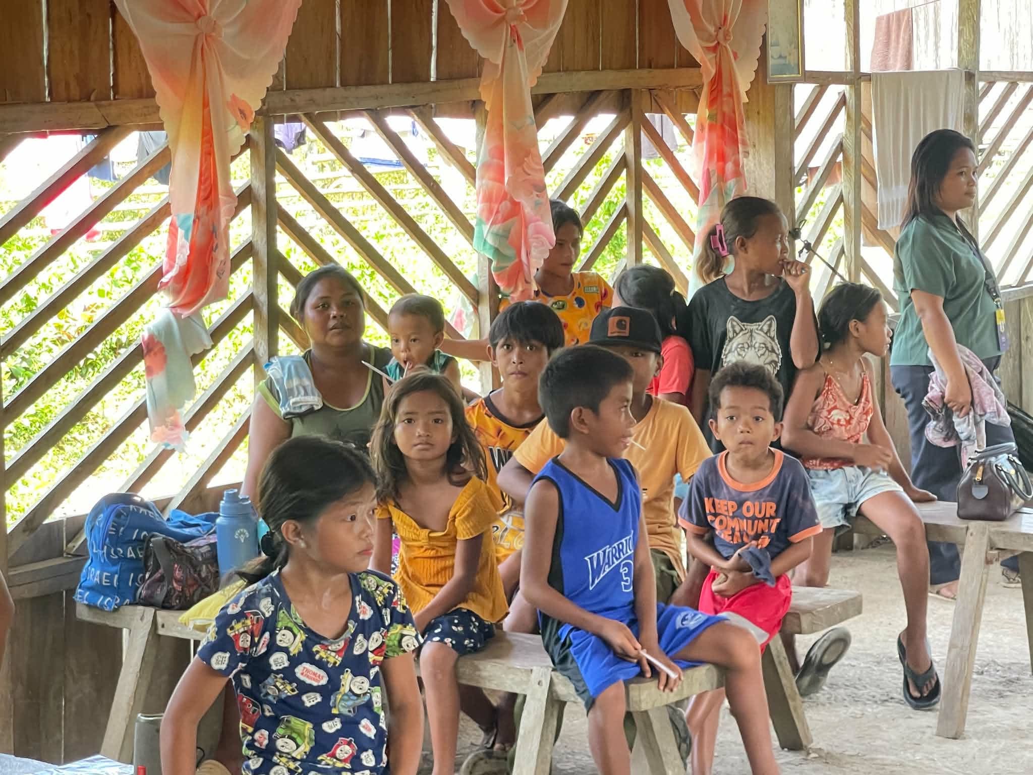 Children and adults seated together inside a wooden shelter