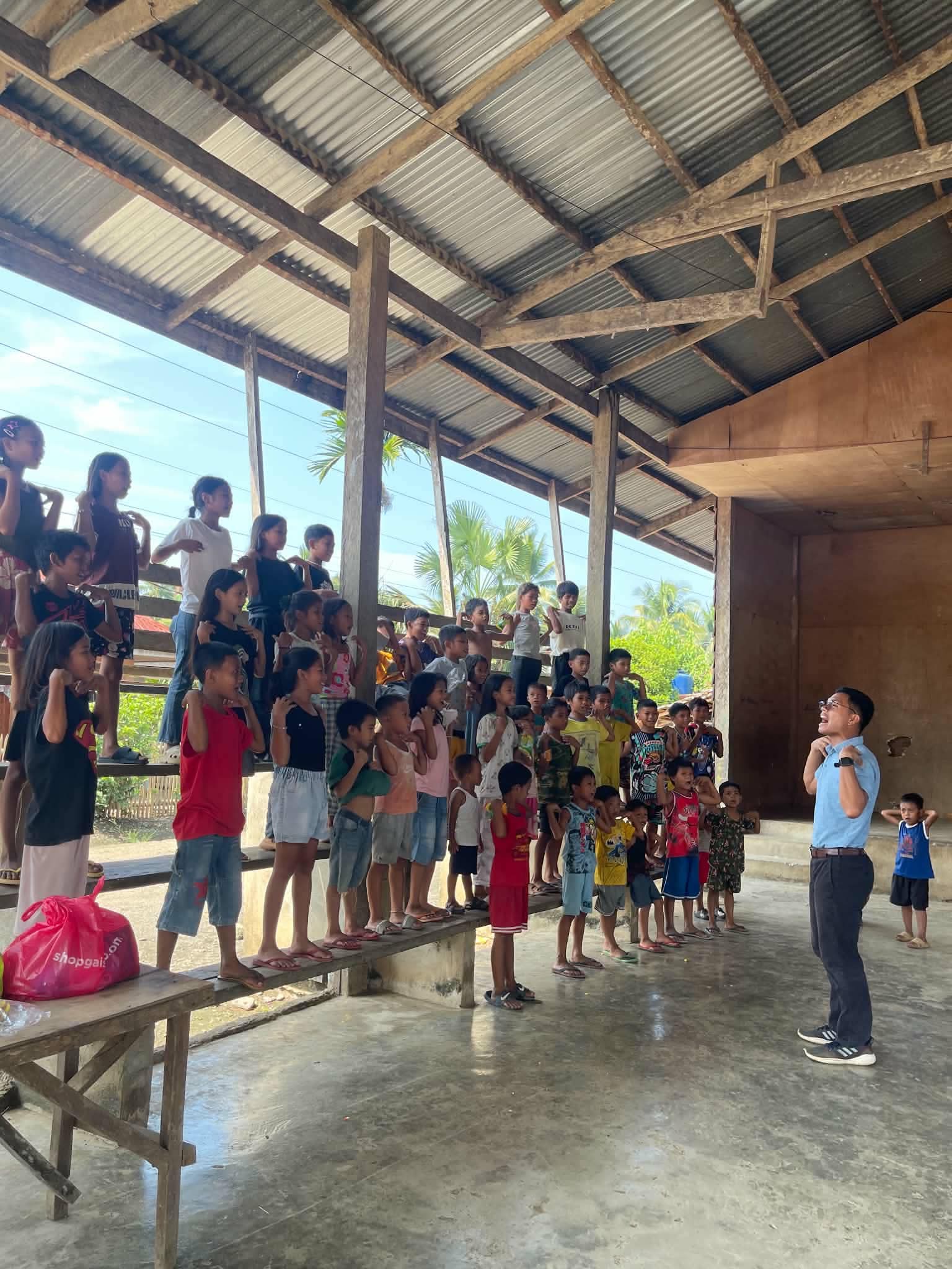 Children standing on benches during a group activity under a metal roof