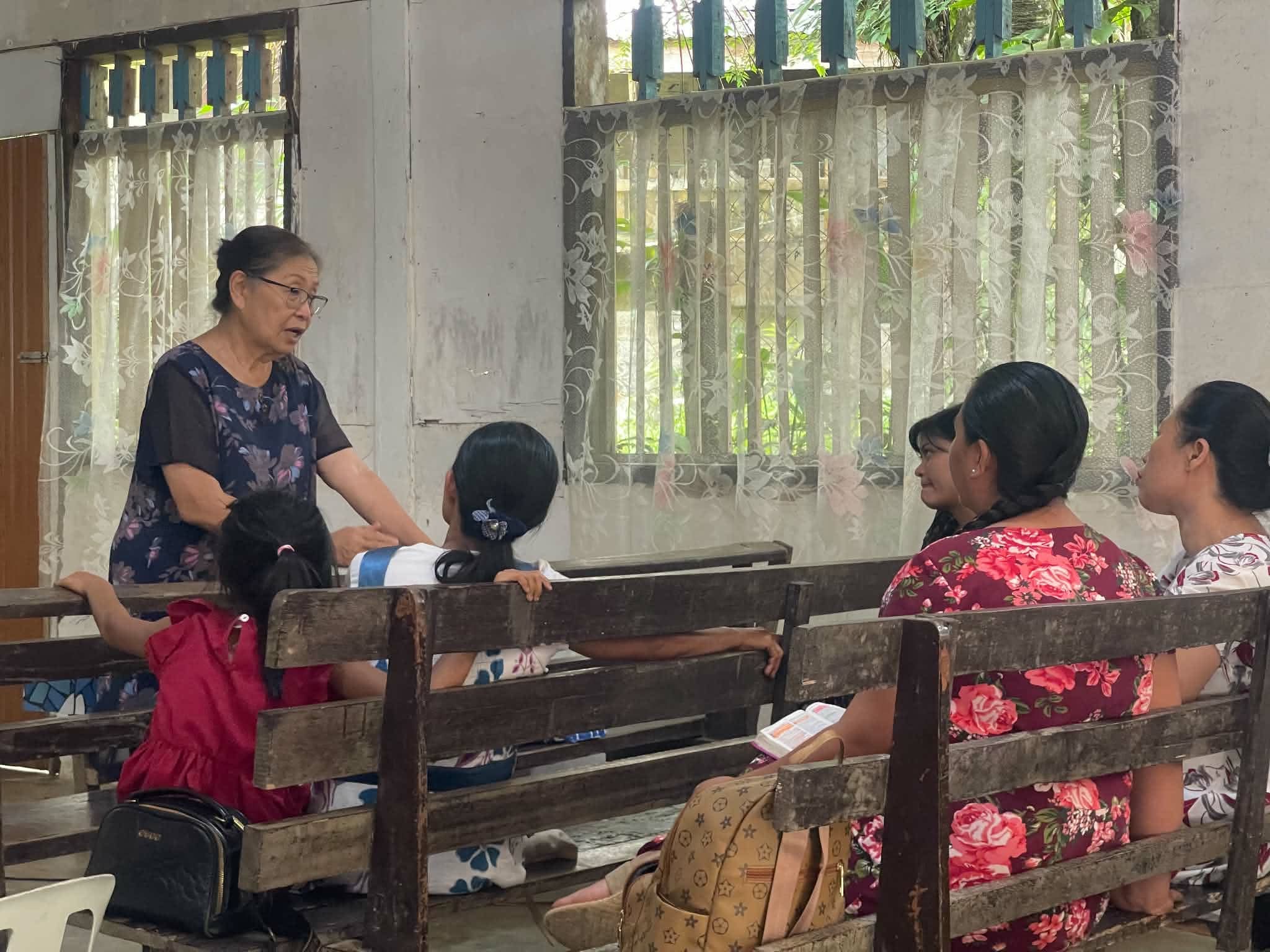 A man speaking with people seated on wooden benches