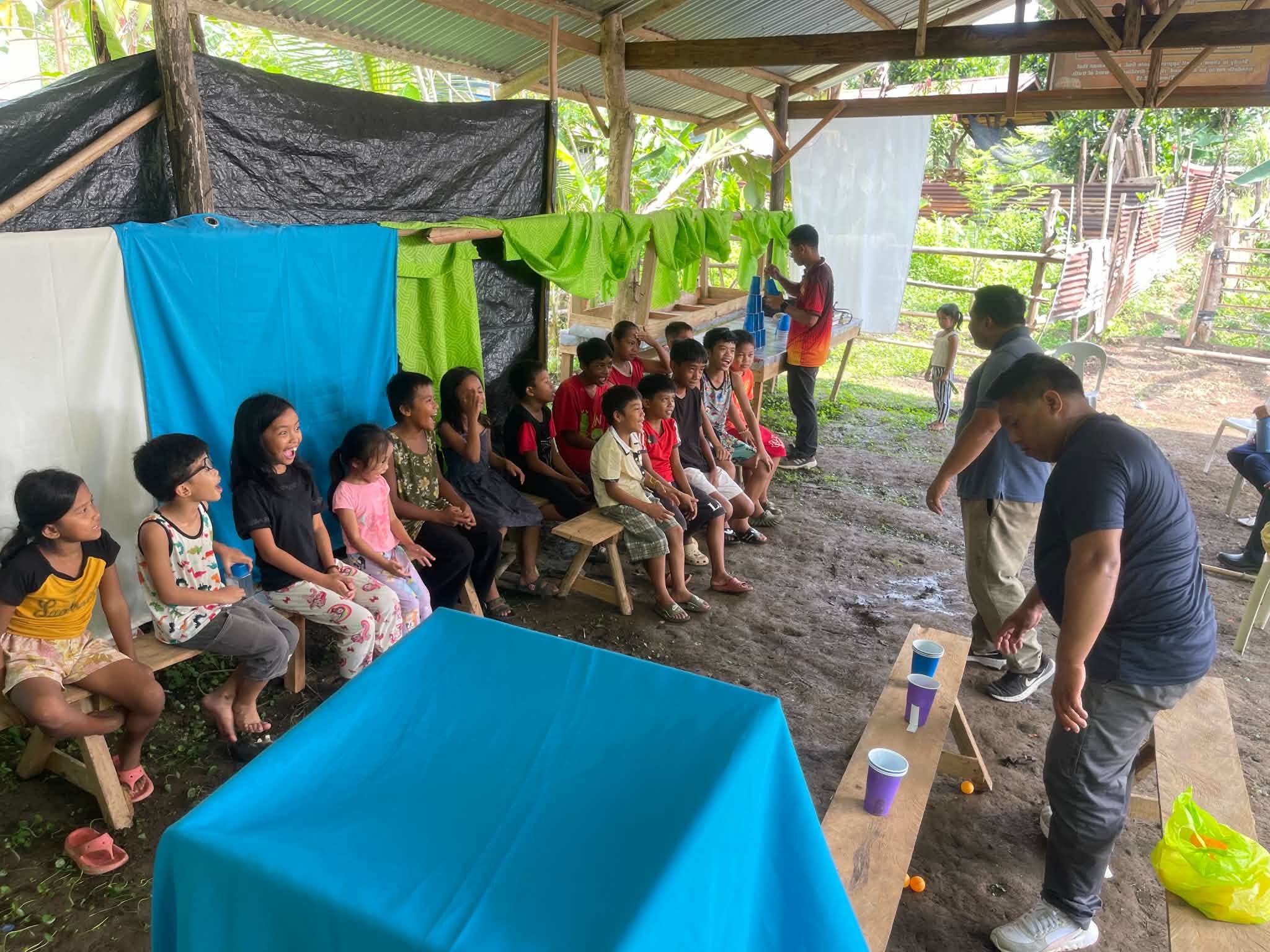 Children seated along a wooden bench while adults lead an activity
