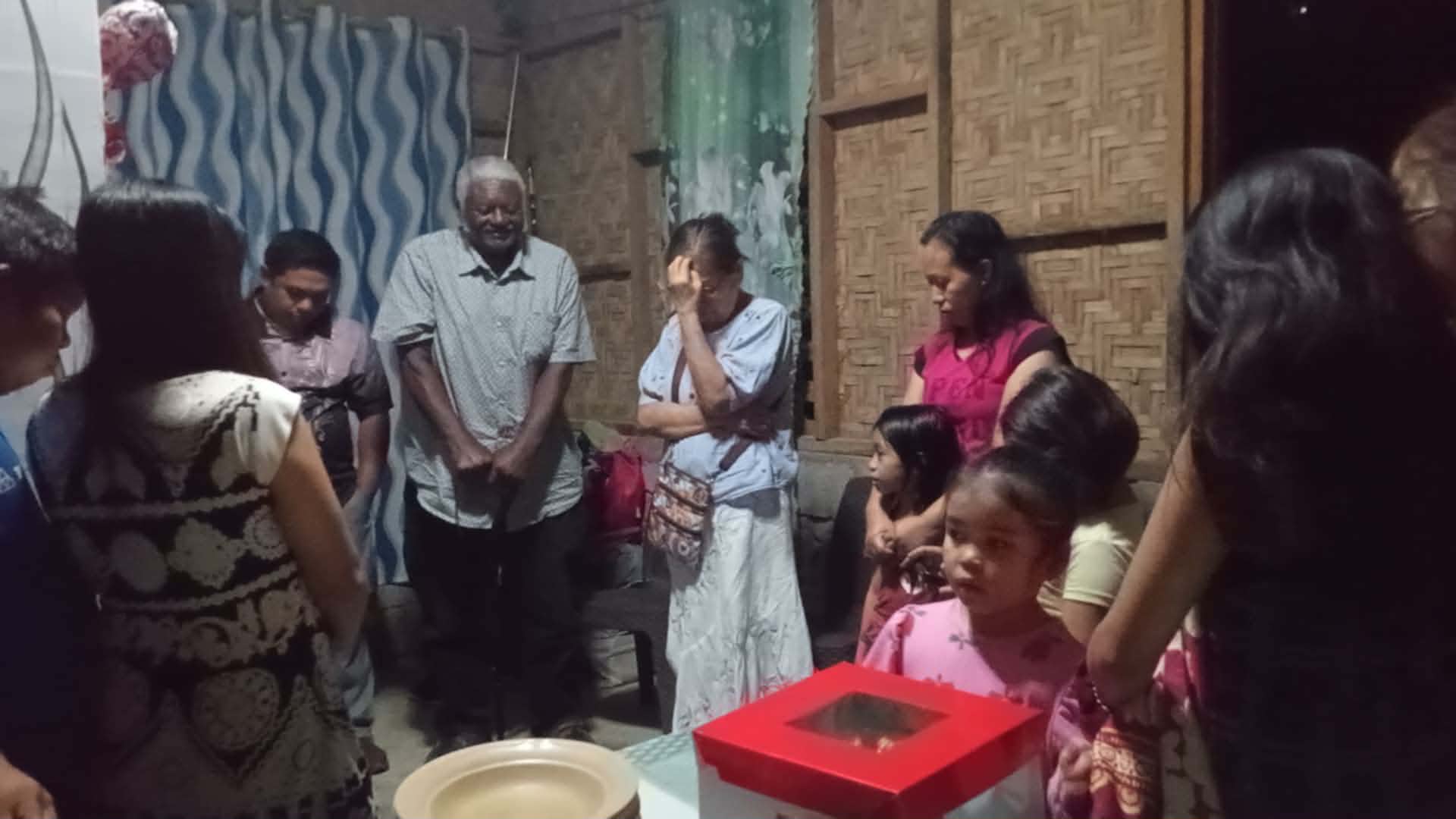 Missionary Henry Walker praying with adults and children inside a family home