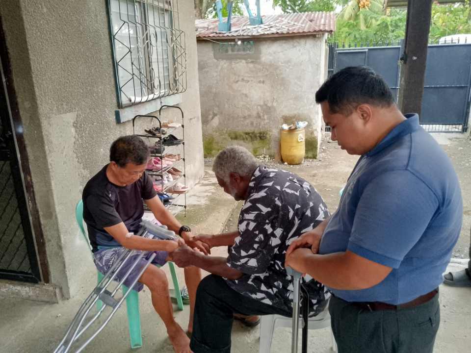 Missionary Henry Walker praying with a church member at his home