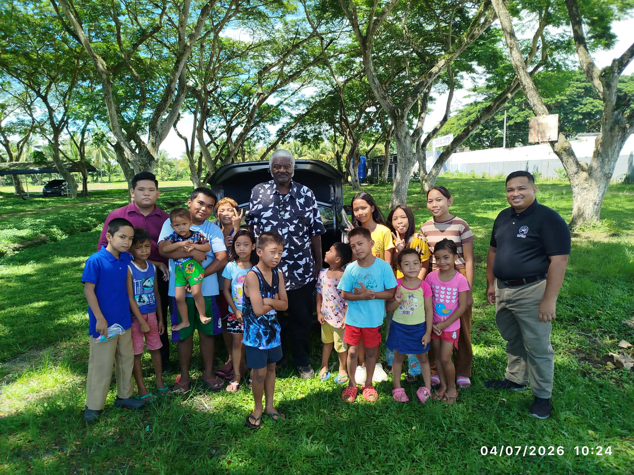 Missionary Henry Walker with children and ministry workers beneath the trees
