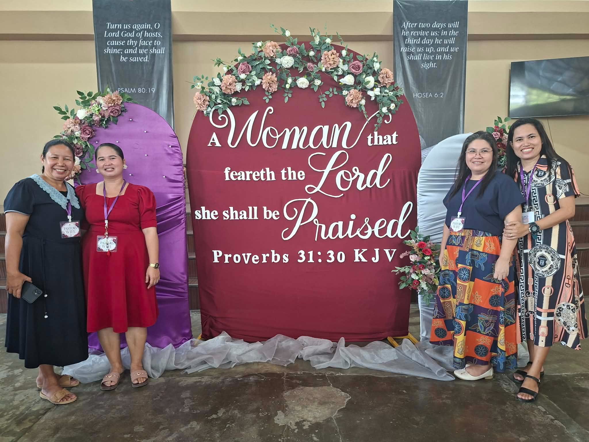Pastors' wives standing beside a Proverbs 31 conference display