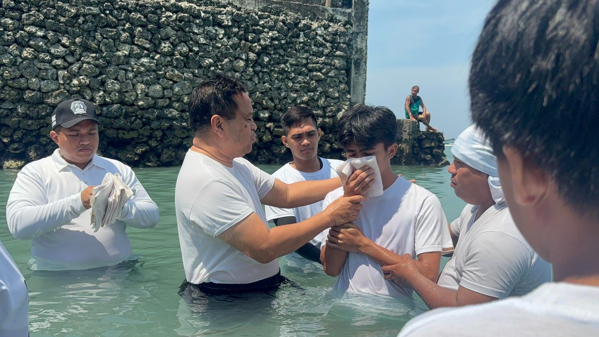 A believer surrounded by church leaders during a water baptism in the sea